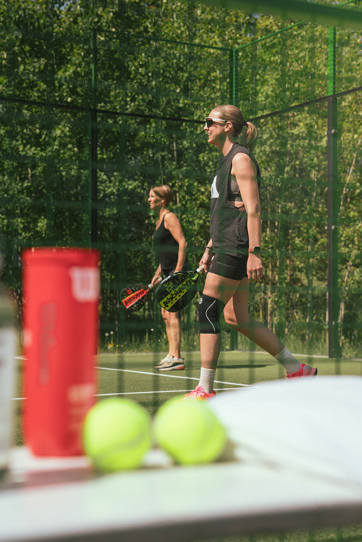 Två kvinnor spelar padel i solen och naturnära omgivningar